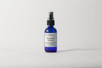 A blue spray bottle of Summer Solace Tallow’s Jasmine Sambac + Magnolia Perfume Mist (Water-Based) UPDATED FORMULA stands upright on a plain white background, with black text highlighting its fresh floral scent and ingredients.