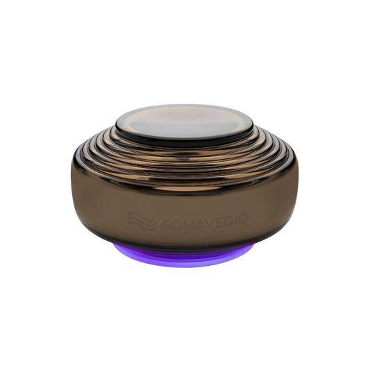Anthracite-colored, dome-shaped electronic device with multiple concentric ridges, a smooth top surface, and a faint purple glow at its base. Designed to mitigate electromagnetic fields (EMF), the brand name "Somavedic USA" is subtly engraved on its side.