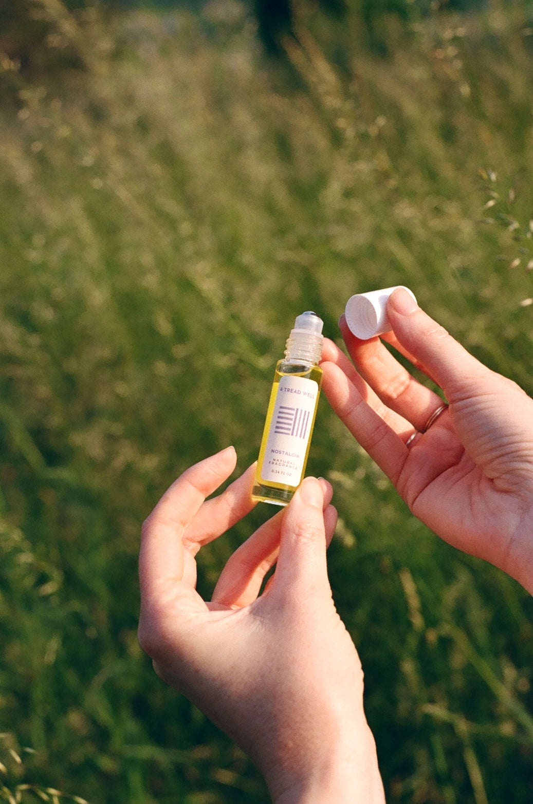 A person stands in a grassy field, holding & Tread Well's Natural Fragrance - Nostalgia with one hand and removing the cap with the other.