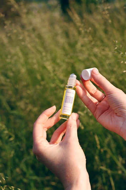 A person stands in a grassy field, holding & Tread Well's Natural Fragrance - Nostalgia with one hand and removing the cap with the other.