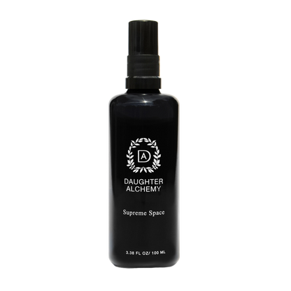 A black spray bottle with a black cap labeled "Daughter Alchemy" and "Supreme Space® Botanical Protective Spray". The bottle also features a circular logo with the letters "DA" in the center. Infused with organic white sage, the volume is listed as 3.38 fl oz / 100 ml.
