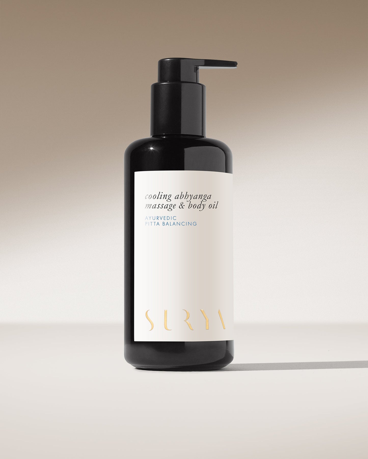 A sleek black bottle with a pump dispenser, labeled "Cooling Body Oil" and "Ayurvedic Pitta Balancing," stands upright against a neutral background. Designed for lymphatic self-massage, the brand name "Surya" shines in gold at the bottom.