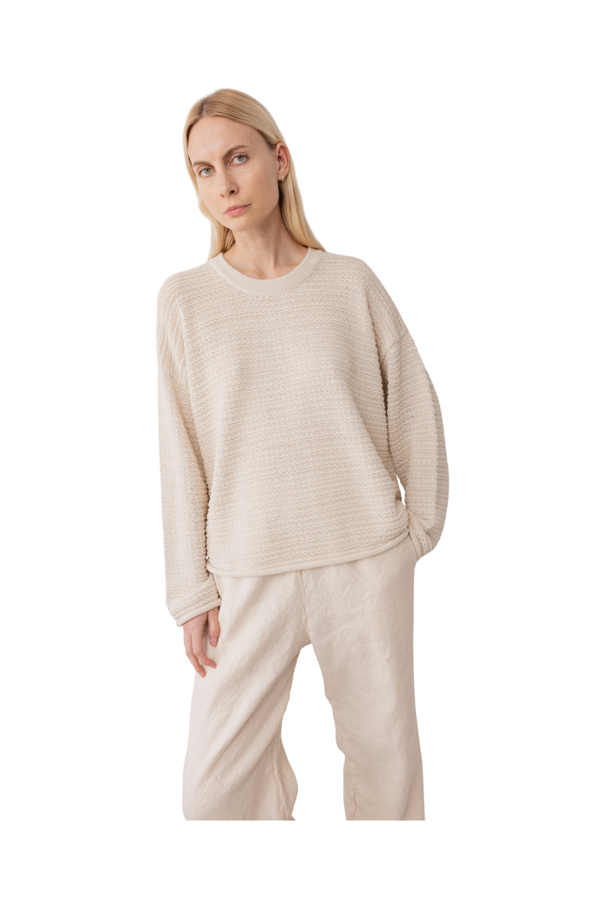 A woman with long blonde hair wears the Wol Hide Thermal Sweater in Natural and wide-leg beige pants, standing against a plain white background and capturing the spirit of slow fashion.