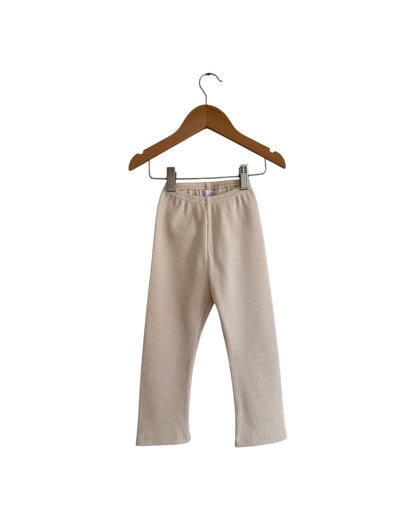 The FAVORIS rib pant by cabane childrenswear is a beige, straight-leg kids’ pant with an elastic waistband, handmade in Vancouver from natural cotton rib, shown on a wooden hanger against a plain white background.