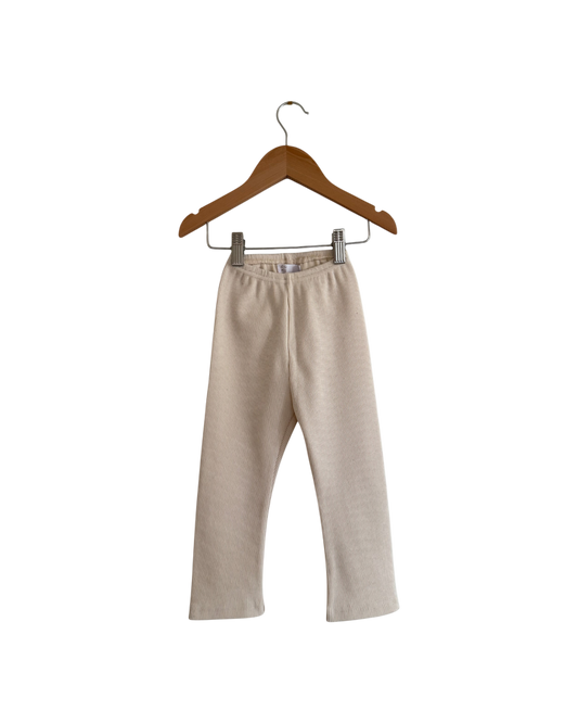 The FAVORIS rib pant by cabane childrenswear is a beige, straight-leg kids’ pant with an elastic waistband, handmade in Vancouver from natural cotton rib, shown on a wooden hanger against a plain white background.