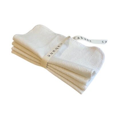 A set of four neatly folded ORGANIC WASHCLOTHS from cabane childrenswear, secured with a white ribbon printed with "cabane" in black letters, shown against a transparent background.