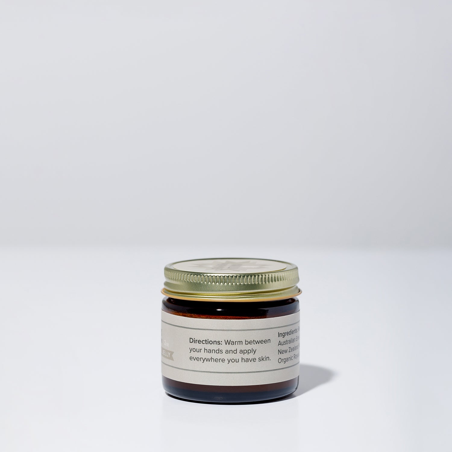 A small brown glass jar with a gold lid and beige label sits on a white surface. The label displays WildMamas' Wildly Nourishing Bison Tallow Balm - Mānuka Honey + Royal Jelly, featuring nutrient-rich tallow for regenerative skincare.