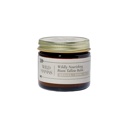 A small amber glass jar with a gold lid labeled "WildMamas Wildly Nourishing Bison Tallow Balm - Mānuka Honey + Royal Jelly." This nutrient-rich balm offers regenerative skincare in a minimalist, cream-colored design.