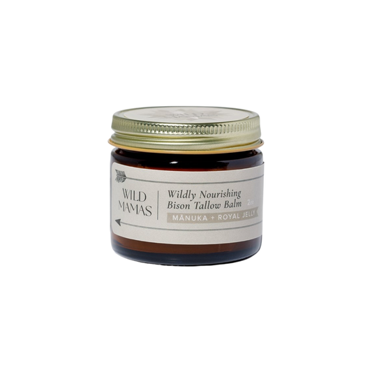 A small amber glass jar with a gold lid labeled "WildMamas Wildly Nourishing Bison Tallow Balm - Mānuka Honey + Royal Jelly." This nutrient-rich balm offers regenerative skincare in a minimalist, cream-colored design.