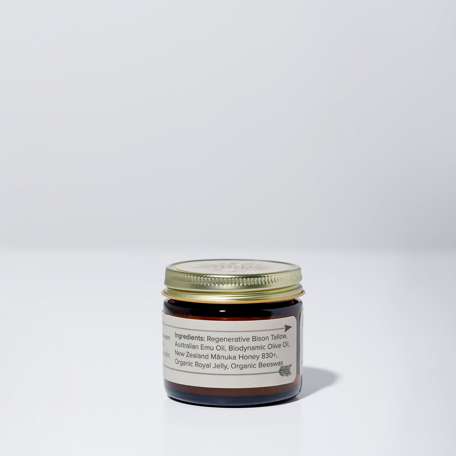 A small brown glass jar with a gold lid from WildMamas sits on a white surface. The label reads: Wildly Nourishing Bison Tallow Balm – Mānuka Honey + Royal Jelly, made with bison tallow, emu oil, olive oil, beeswax, and more.