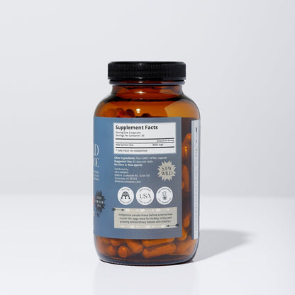 A brown glass bottle with a black lid contains orange WildMamas Wild Salmon Roe capsules. The label shows supplement facts, certifications, and icons for vegan, made in the USA, and "Stay Wild." The bottle is on a plain white background.