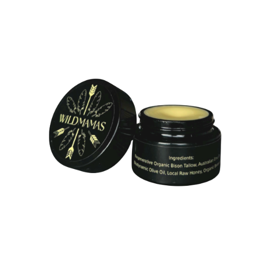 An open small black jar of Wild Mamas' Wildly Nourishing Bison Tallow Balm – Raw Honey, with an illustrated lid of leaves and feathers. Yellow balm is visible inside, and ingredients appear in white text on the side.