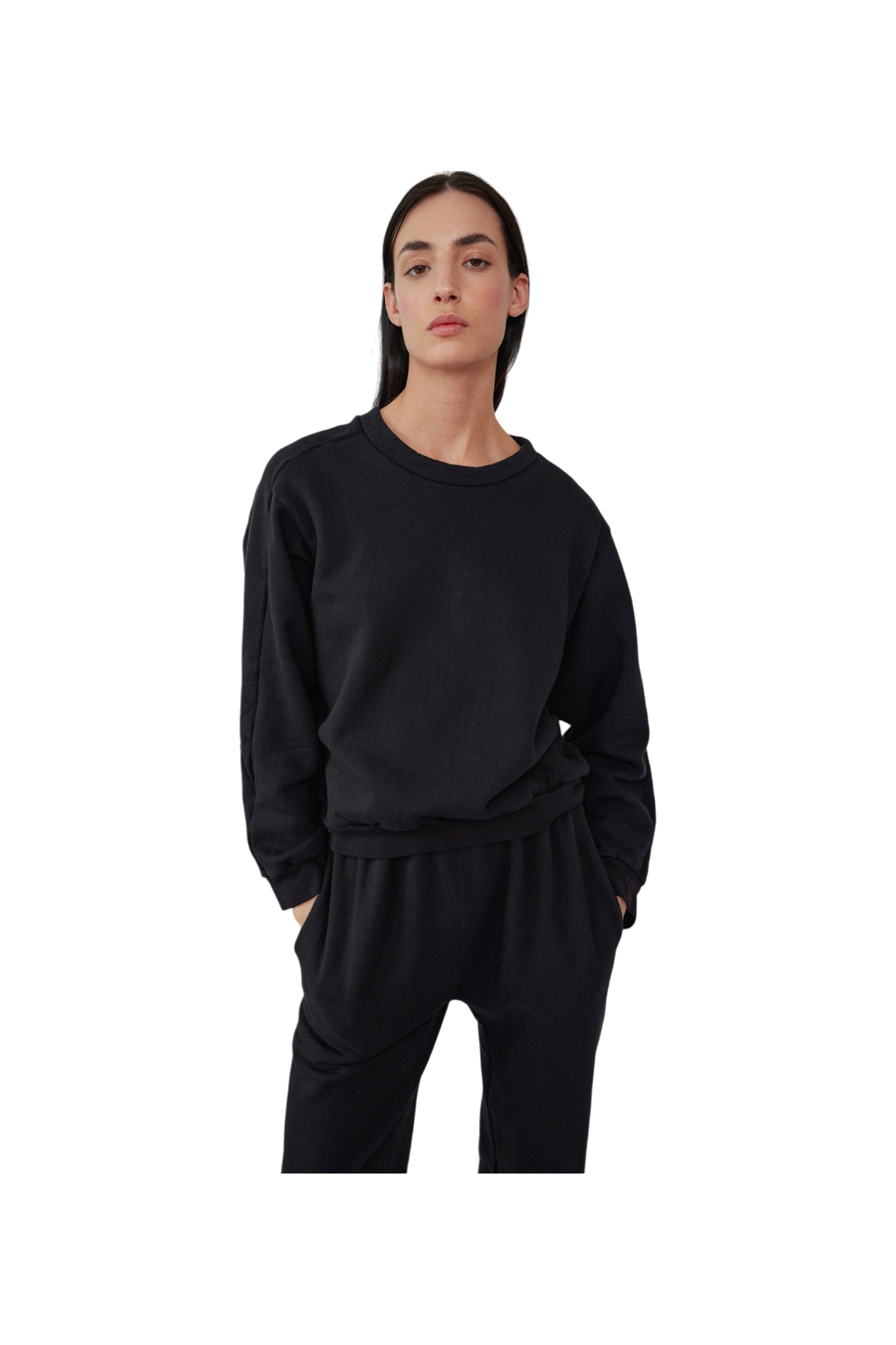Against a black background, a person dons the Easy Winter Sweatshirt in black by Wol Hide. Crafted from organic cotton fleece, this boxy crew neck sweatshirt is perfectly paired with matching pants. With hands casually tucked into their pockets and wearing a neutral expression, this ensemble highlights understated elegance and exceptional craftsmanship, proudly made in the USA.