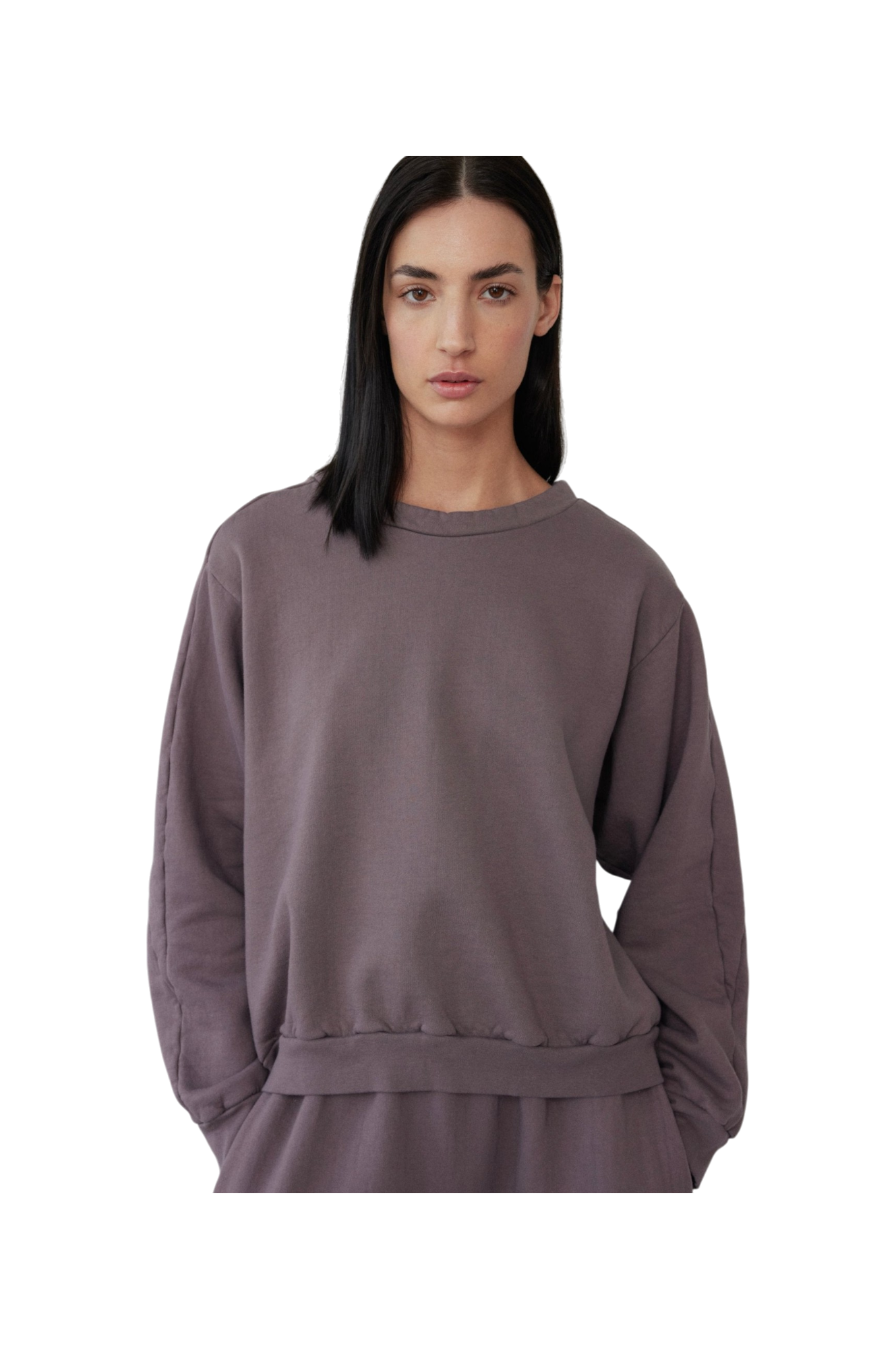 A person with long, dark hair is wearing the Wol Hide Easy Winter Sweatshirt in Mushroom, made in the USA. Their hands are tucked into matching pants crafted from 100% organic cotton. The background is plain and black.