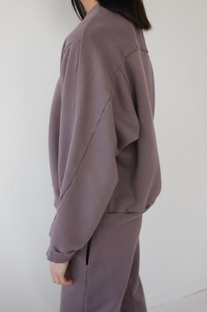 A person wearing the Wol Hide Easy Winter Sweatshirt in Mushroom stands sideways against a plain, light background. This loose-fitting, organic cotton crew neck tracksuit is made in the USA and effortlessly combines style with sustainability.