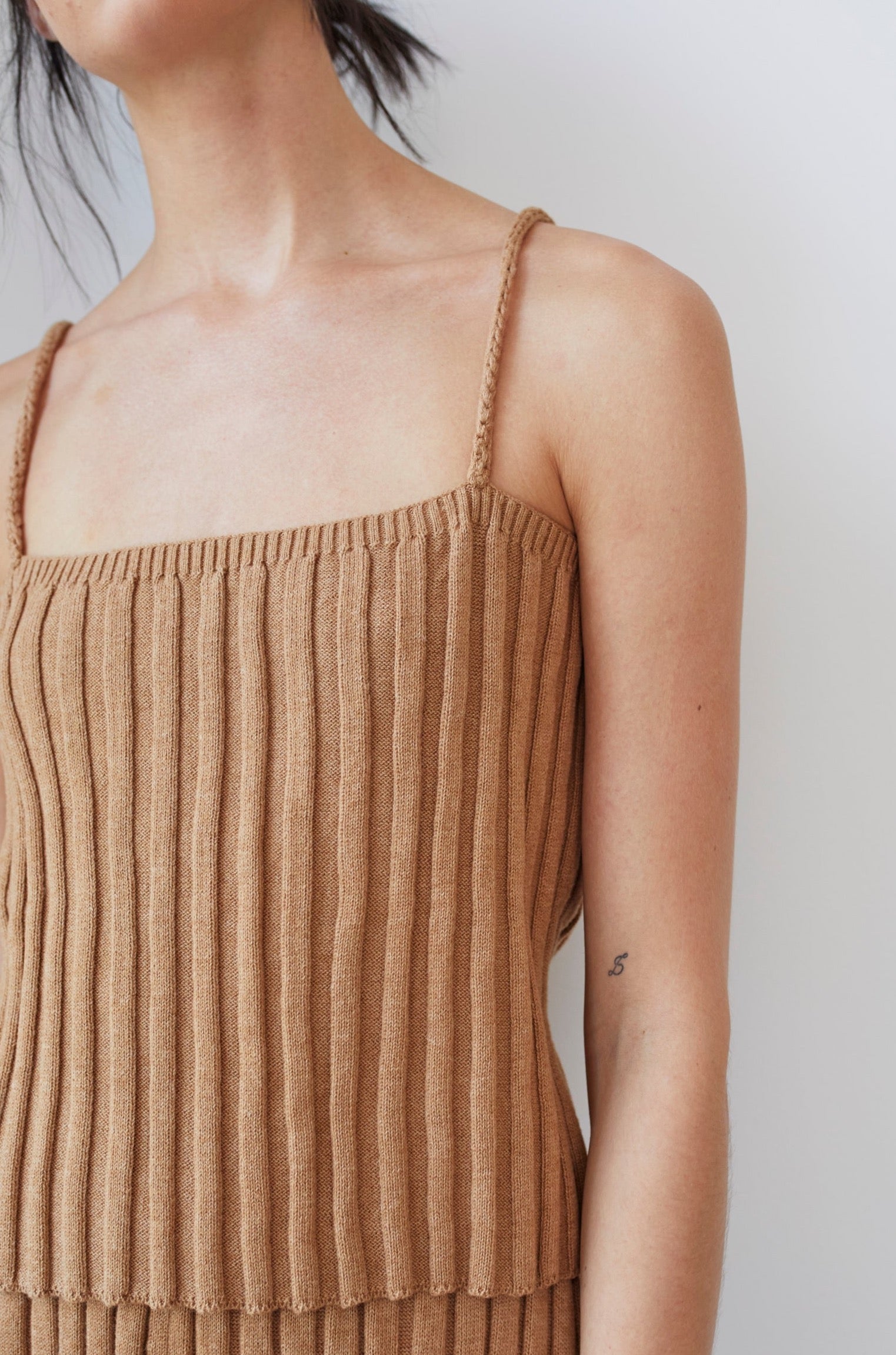 A person showcases the Wol Hide Organic Cotton Rib Cami in Toffee against a plain background, revealing only their shoulder and upper torso with a small tattoo visible on their arm.