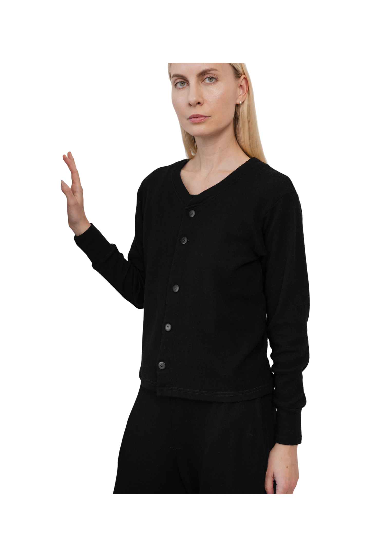 A woman with straight blonde hair models the Wol Hide Wool Liner in Onyx—a minimalist black cardigan—paired with black pants against a white background, showcasing a modern, sustainable style as she raises her left hand.