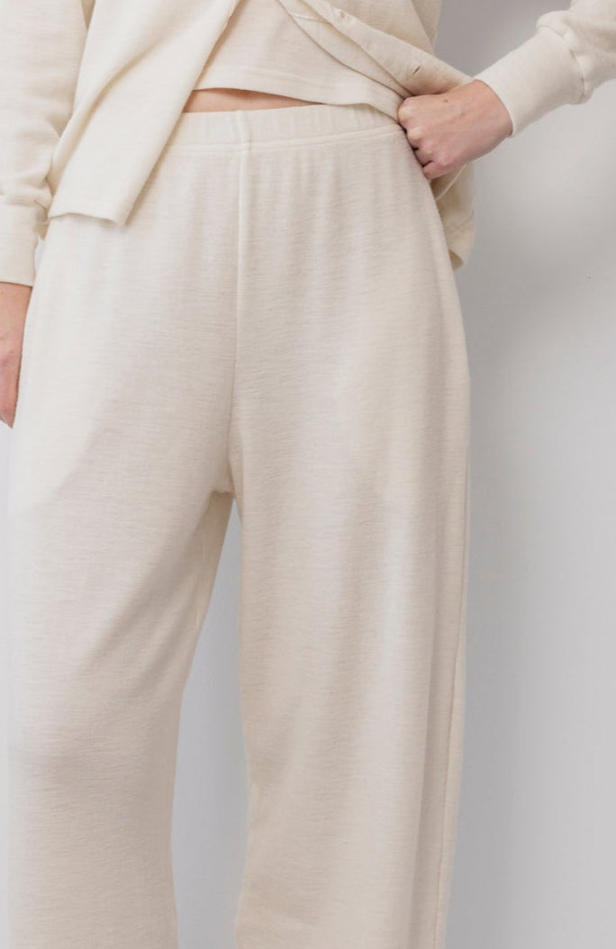 A person wears Wol Hide's Wool Wide Leg: Natural pants—cream-colored, wide leg with an elastic waist—paired with a matching top. The visible lower torso and upper legs highlight the outfit's soft, comfortable look. One hand rests on their hip.
