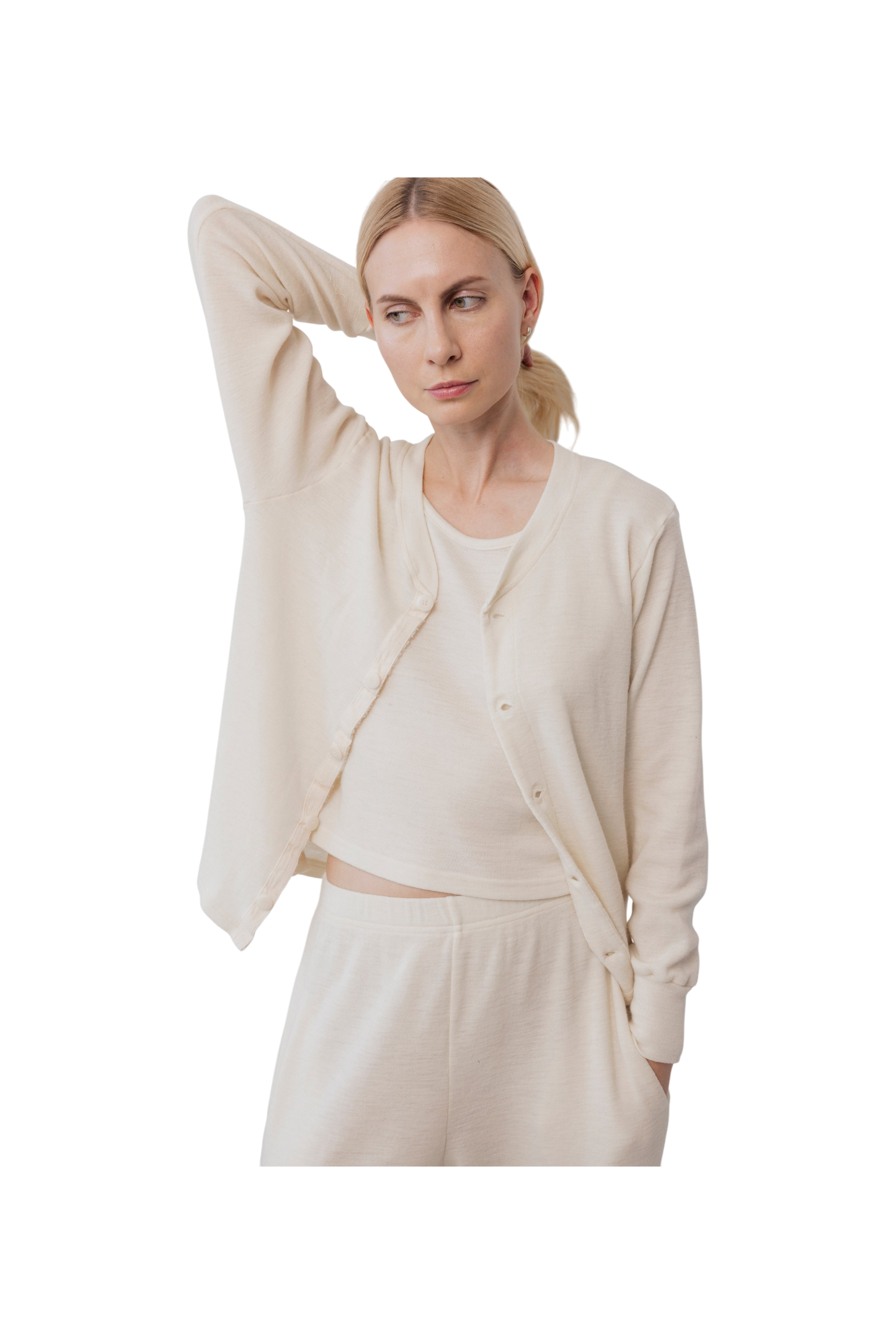 A woman in cream Wol Hide Wool Liner loungewear stands with one hand behind her head, looking to the side. She wears a matching set that embodies minimalist style against a plain white background.