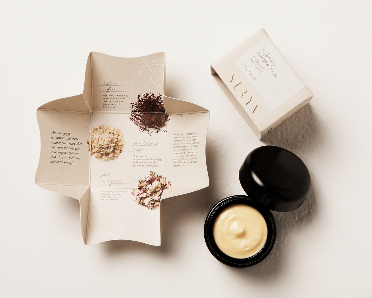 A cream product in a black container with its lid open is displayed next to an unfolded product brochure. The brochure contains detailed information and illustrations of the natural ingredients in this botanical retinol formula. A closed box with the brand name "Surya" is also visible, indicating that this is the Balancing Collagen Cream.