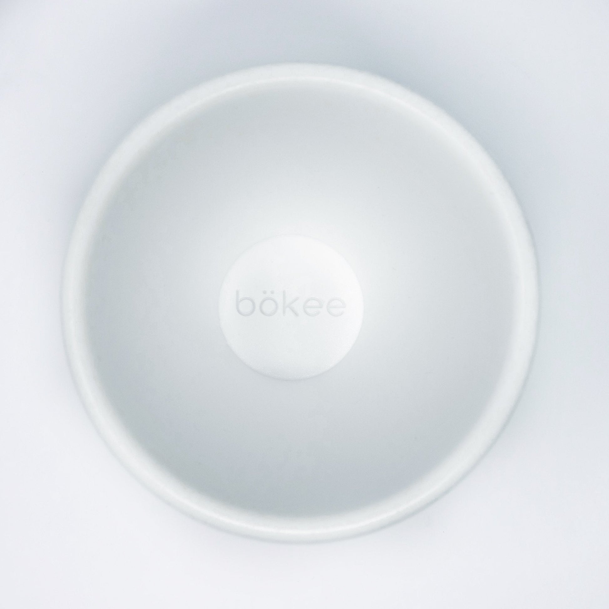 Top view of the "bökee Baby Bottle Holder, One-Handed Bottle Prep," a white, circular product crafted from BPA-free silicone designed to hold and stabilize baby bottles during one-handed bottle preparation. The smooth, minimalist design prominently features the brand name "bökee" in the center.