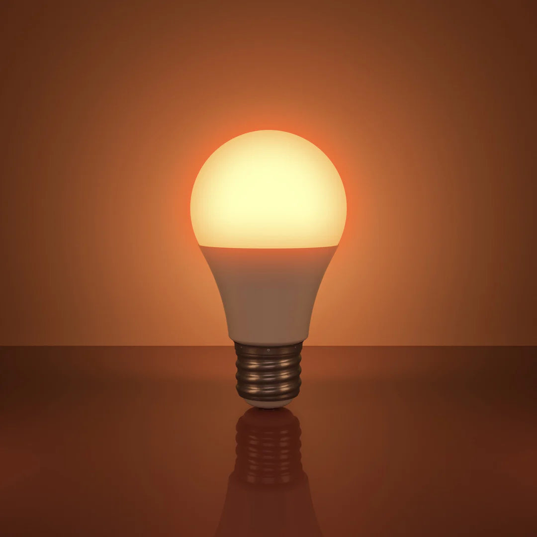 The Healthy Home Shop's Circadian Lightbulb stands upright on a reflective surface against a warm orange background, emitting a gentle glow of circadian-friendly light.