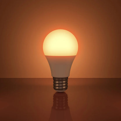 The Healthy Home Shop's Circadian Lightbulb stands upright on a reflective surface against a warm orange background, emitting a gentle glow of circadian-friendly light.