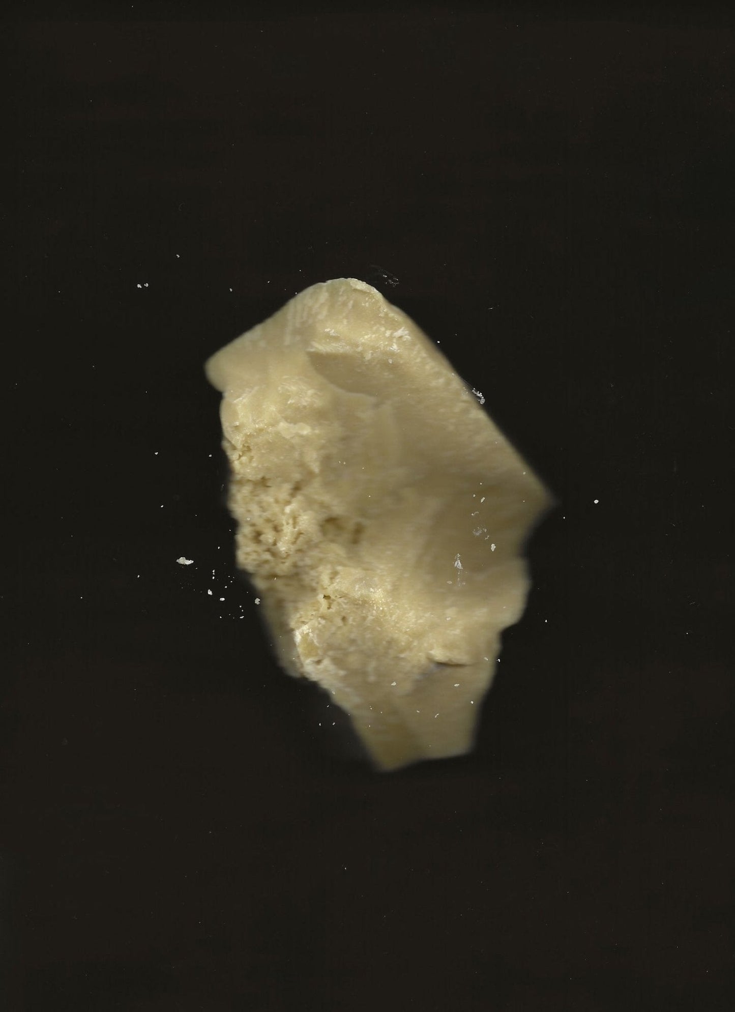 A partially bitten chunk of Cacao Rose Cuticle, Lip, and Brow Balm - Regenerative Tallow™ from Summer Solace Tallow, floating against a dark background. The off-white balm has a crumbly texture, with smaller pieces breaking off around it.