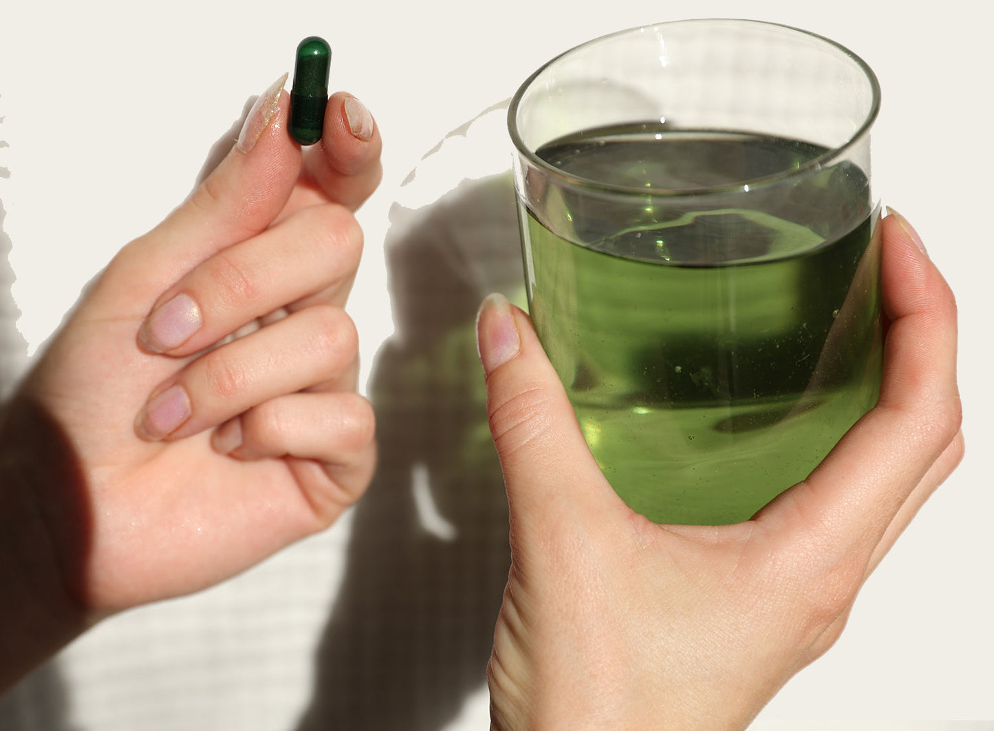 A person holding Juna's Gut Therapy Supplement, a green capsule emphasizing gut health, in their right hand and a clear glass of green liquid to boost metabolism in their left hand, against a light background.