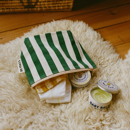 Dr. Max's Baby Essentials Bundle features a green and white striped pouch, partly open to reveal a folded cloth, alongside two tins labeled "Diaper Ointment" and "Baby Balm," one open to show the gentle yellow balm inside.