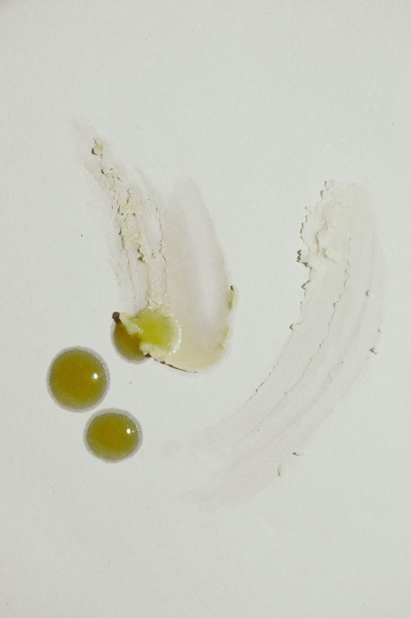 Three greenish-yellow blobs and a pale smear of Emanations Profound Face Oil by Summer Solace Tallow create an abstract pattern on a white surface, highlighting its nourishing blend of Champa, Tuberose & White Ginger Lily.