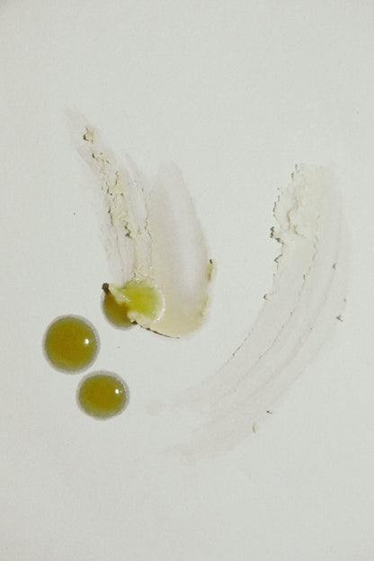 Three greenish-yellow blobs and a pale smear of Emanations Profound Face Oil by Summer Solace Tallow create an abstract pattern on a white surface, highlighting its nourishing blend of Champa, Tuberose & White Ginger Lily.