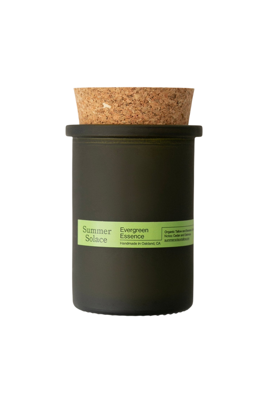 The Summer Solace Tallow Evergreen Essence (Cedar and Oakmoss) Candle is a handmade, dark green glass jar candle with a cork lid. Crafted in Oakland, CA, it features a woodsy forest scent and uses Regenerative Tallow® with organic ingredients.