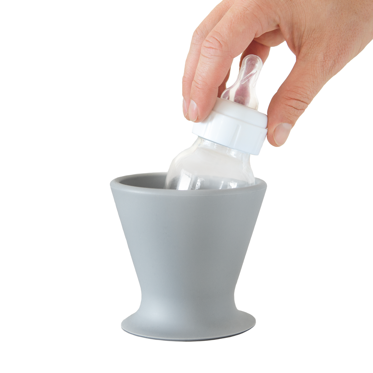 A hand places a BPA-free silicone baby bottle into a gray bökee Baby Bottle Holder. The holder, designed by bökee, boasts a wide, conical shape and features a simple, modern design ideal for one-handed bottle preparation. The bottle is equipped with a white cap and clear nipple.