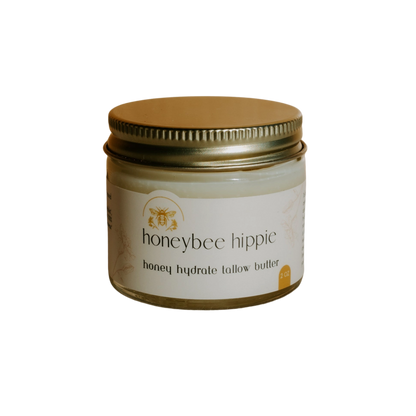The small jar with a gold lid features "honey hydrate tallow butter" from Honeybee Hippie. With a bee illustration on its label, set against black, it exudes organic charm and promises natural nourishment.