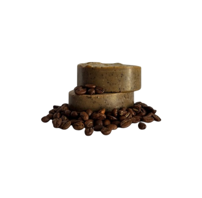 Two Wild Bison Tallow Deep Exfoliating Soap Scrub bars (Shilajit + Decaffeinated Coffee Bean) from Wild Mamas are stacked on whole coffee beans, set against a plain white background—ideal for fans of a rich coffee scrub.