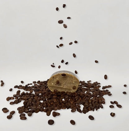 A small wooden barrel spills dark decaf coffee beans—just like those in our Wild Mamas Wild Bison Tallow Deep Exfoliating Soap Scrub with Shilajit—scattered on a white background, with more beans falling from above.