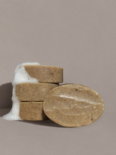 Three round, tan Wild Mamas Wild Bison Tallow Gentle Exfoliating Soap Scrub bars (Madagascar Vanilla Bean + Manuka Honey) are stacked with white foam nearby. A fourth bar leans against the stack, set on a plain beige background.