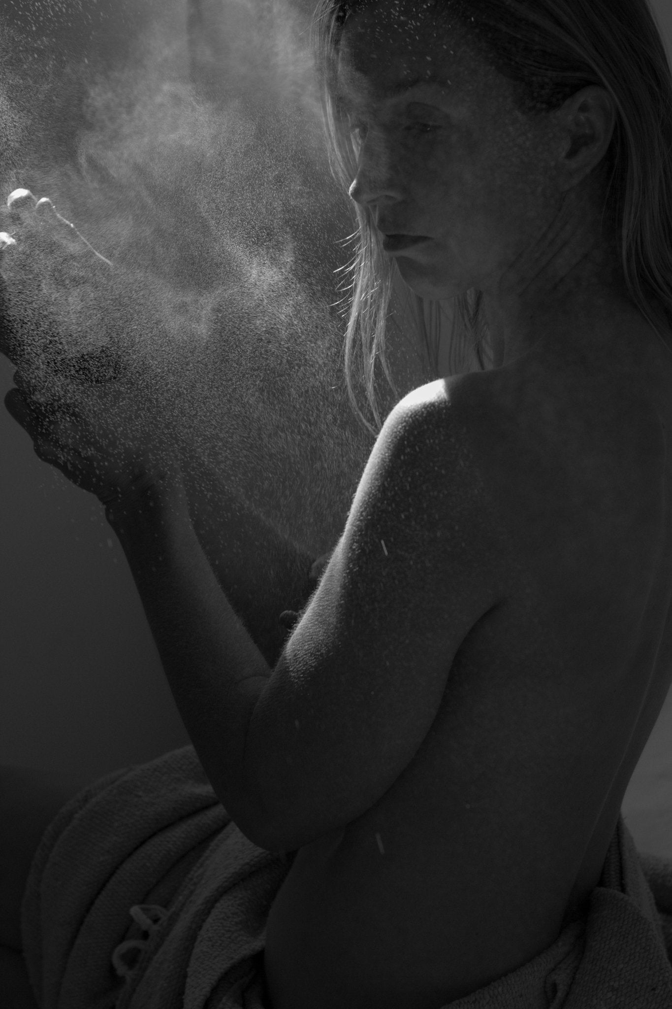 A black and white photo of a topless person with long hair, wrapped in a towel and surrounded by swirling powder, captures the airy elegance of Summer Solace Tallow's Jasmine Sambac + Magnolia perfume mist (water-based), updated formula.