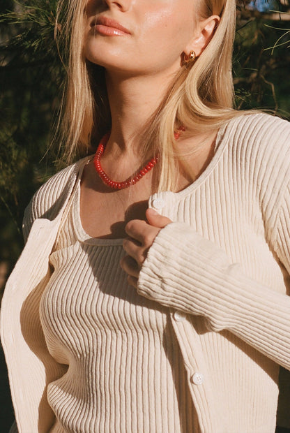 Natural 
A woman with long blonde hair wears the LA Relaxed Pointelle Square Cami under a cream rib cardigan and a beaded necklace while standing outdoors in natural light, partially facing the camera.