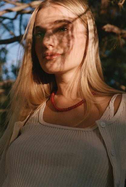 Natural A woman with long blonde hair wears the LA Relaxed Pointelle Square Cami, a ribbed vintage-inspired top. She stands outdoors, sunlight and tree shadows playing across her face and shoulders.