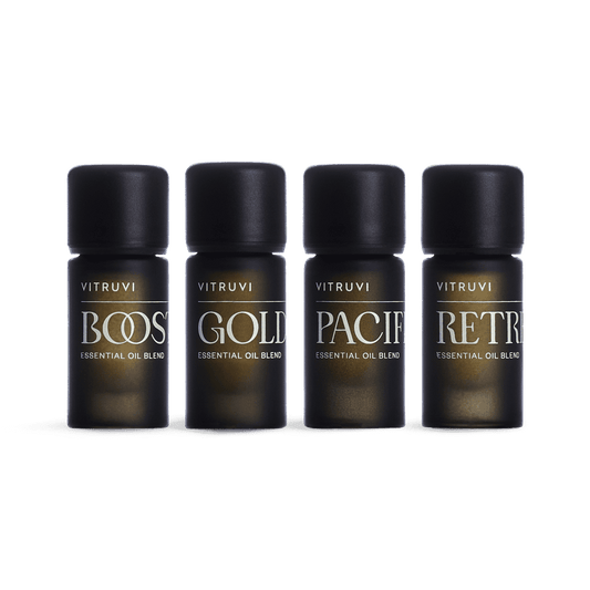 The Vitruvi Refresh Diffuser Blend Kit showcases four small, dark bottles of revitalizing essential oil blends, neatly lined up. Each bottle is labeled with the names "BOOST," "GOLD," "PACIFIC," and "RETREAT." With black caps set against a white background, these oils are designed to invigorate your atmosphere.