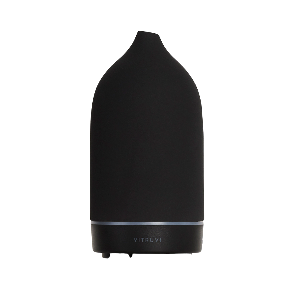 Introducing the Stone Diffuser by Vitruvi, a sleek black essential oil diffuser with a modern, minimalist design. This elegant piece features a smooth, conical shape with a small opening at the top, ideal for pure essential oils. The brand name "Vitruvi" is gracefully displayed on the lower part of the unit, making it an exquisite addition to any home decor.