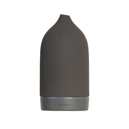 The Vitruvi Stone Diffuser features a sleek, black matte finish with a modern, minimalist design. Its slightly tapered top and smooth surface add to its elegant aesthetic. The brand name "VITRUVI" is subtly embossed near the base, making it an exquisite addition to your home decor for using pure essential oils.