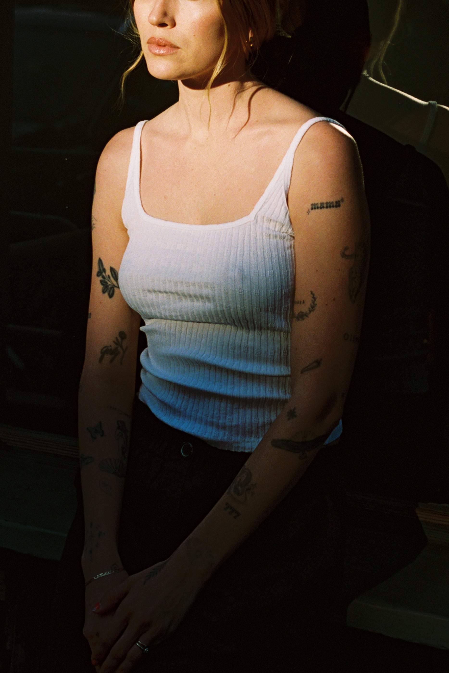 White 
A woman with tattoos on her arms wears the LA Relaxed Pointelle Square Cami and dark pants, standing partially in shadow with her hands clasped. Her face is partly out of the frame.