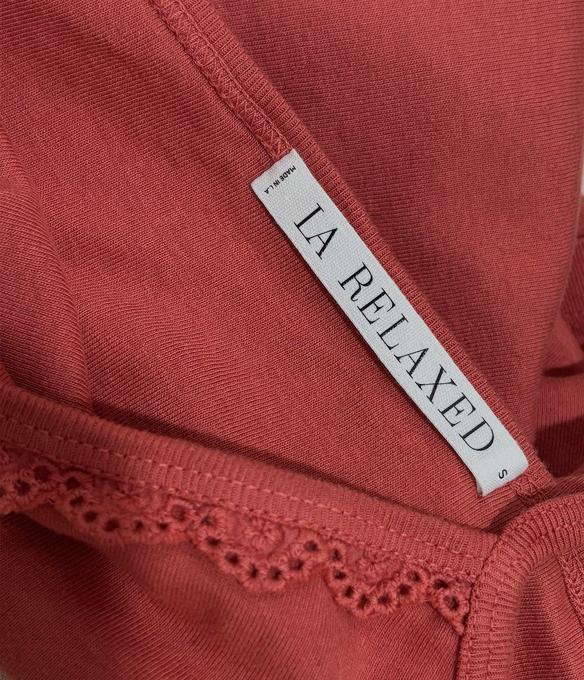 Rose - Close-up of the Frill Camisole by LA RELAXED in pink, size S. Made from soft organic cotton, it features a visible tag and elegant lace trim along the edge.