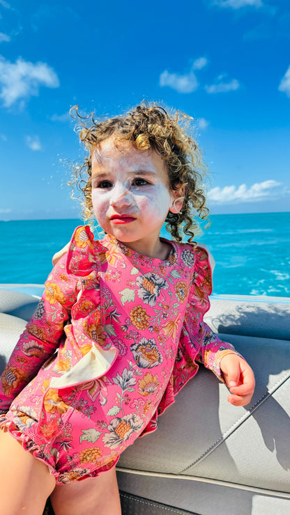 A curly-haired child wearing a pink floral swimsuit sits on a boat, enjoying the turquoise ocean while using Wild Mamas Wildly Nourishing Bison Tallow Balm - Sunscreen, a natural powerhouse for regenerative skincare.