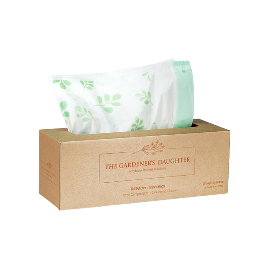 A brown rectangular box labeled "The Gardener's Daughter" presents eco-friendly 13-gallon compostable trash bags with green text. One white bag, decorated with green leaf patterns, is partially pulled from the 100%-certified pack.