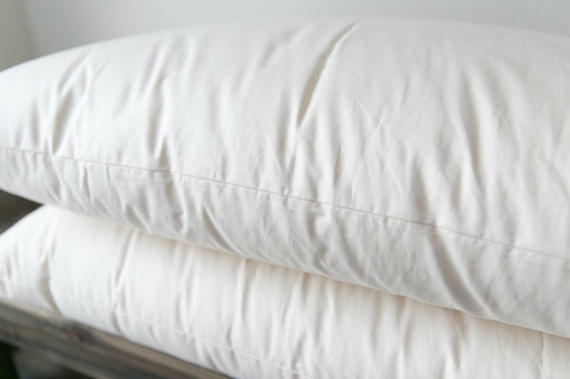 A close-up of two Ashland Organic Wool Pillows by Shepherd's Dream stacked on a wooden surface. These pillows feature a smooth texture, indicating they are clean and freshly laundered, making them ideal for a healthy bed and natural sleep environment.