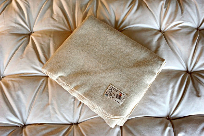 A folded Shepherd's Dream wool mattress protector with a beige label on top, placed on a tufted surface.